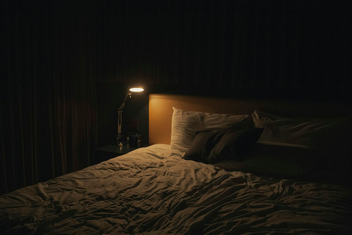 A bedside lamp glowing beside an unmade bed at night