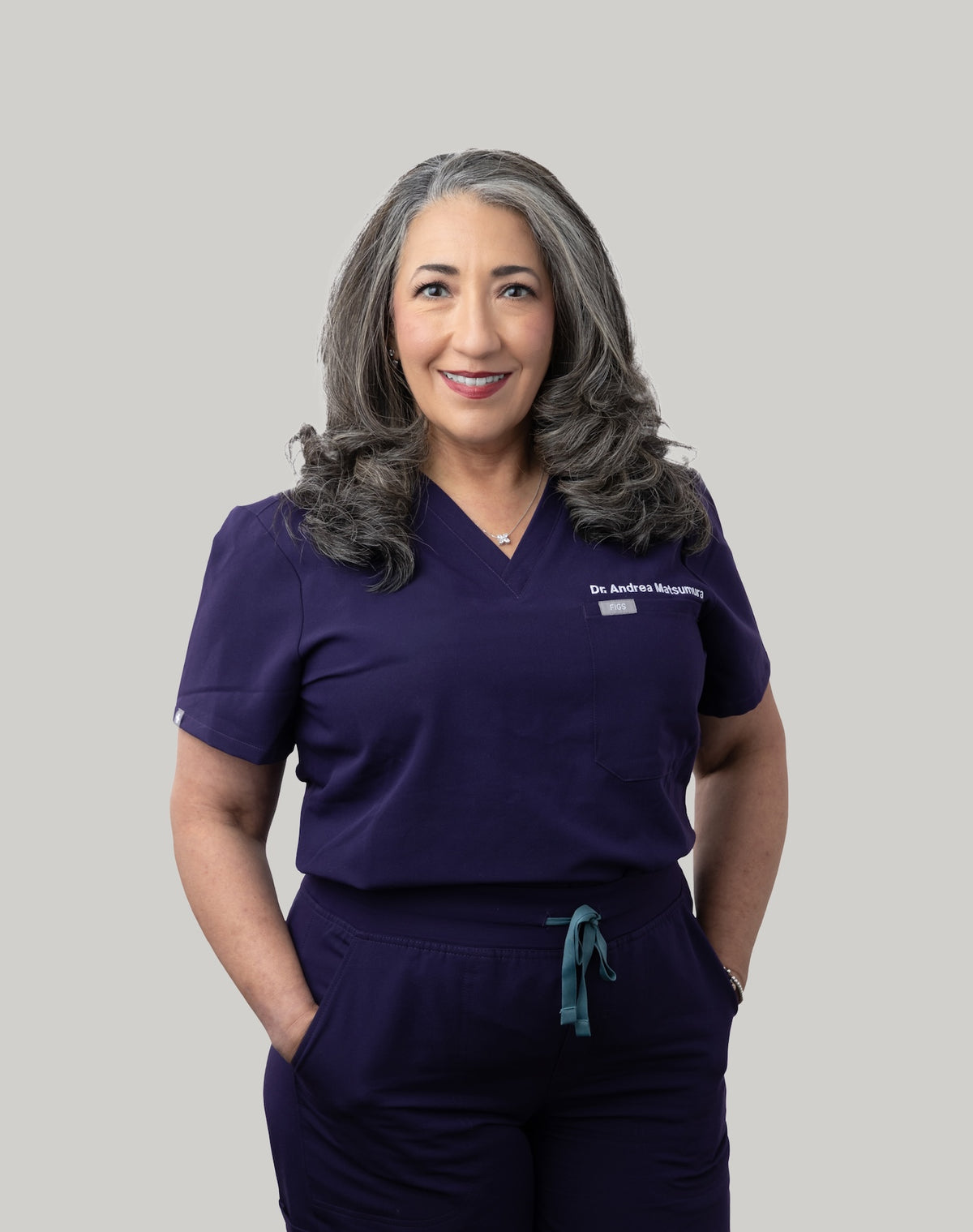 Dr. Andrea Matsumura wearing a purple medical scrub set with 'Dr. Andrews' embroidered on the shirt.