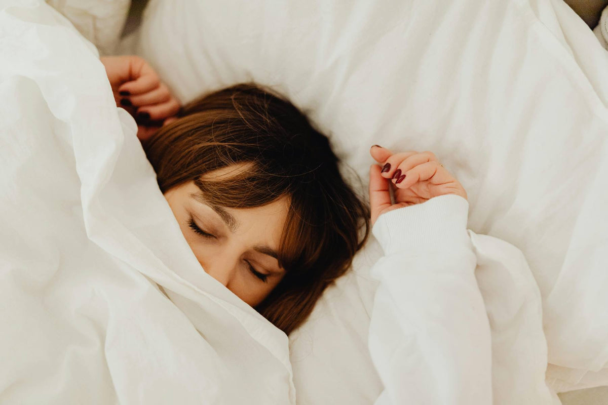 Person lying in bed under white sheets and blanket