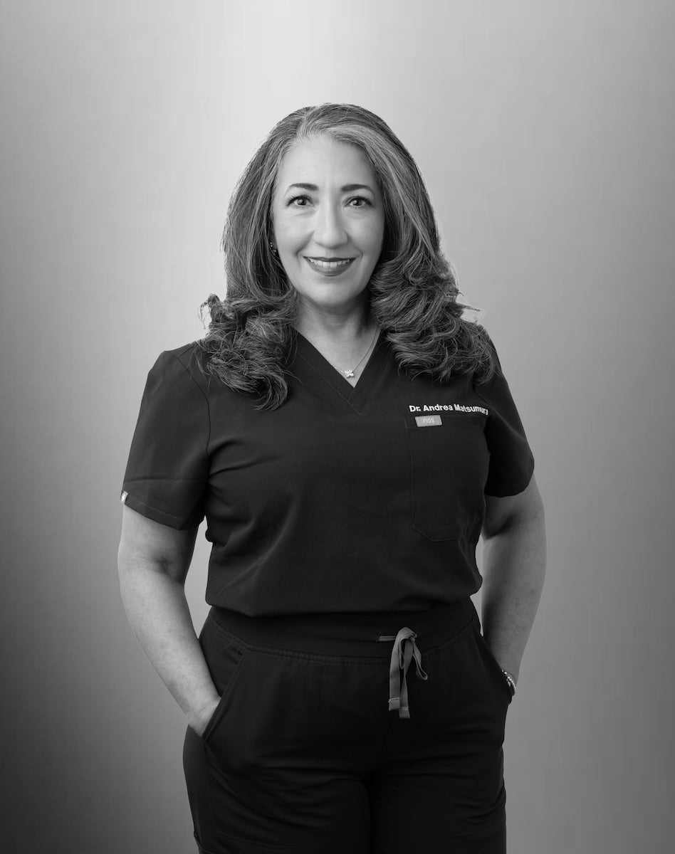 Dr. Andrea Matsumura wearing a black scrub top with a name tag on a gray background