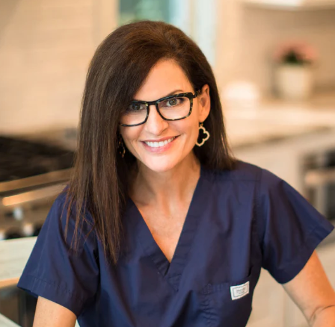 Woman wearing navy scrubs and glasses in a kitchen setting