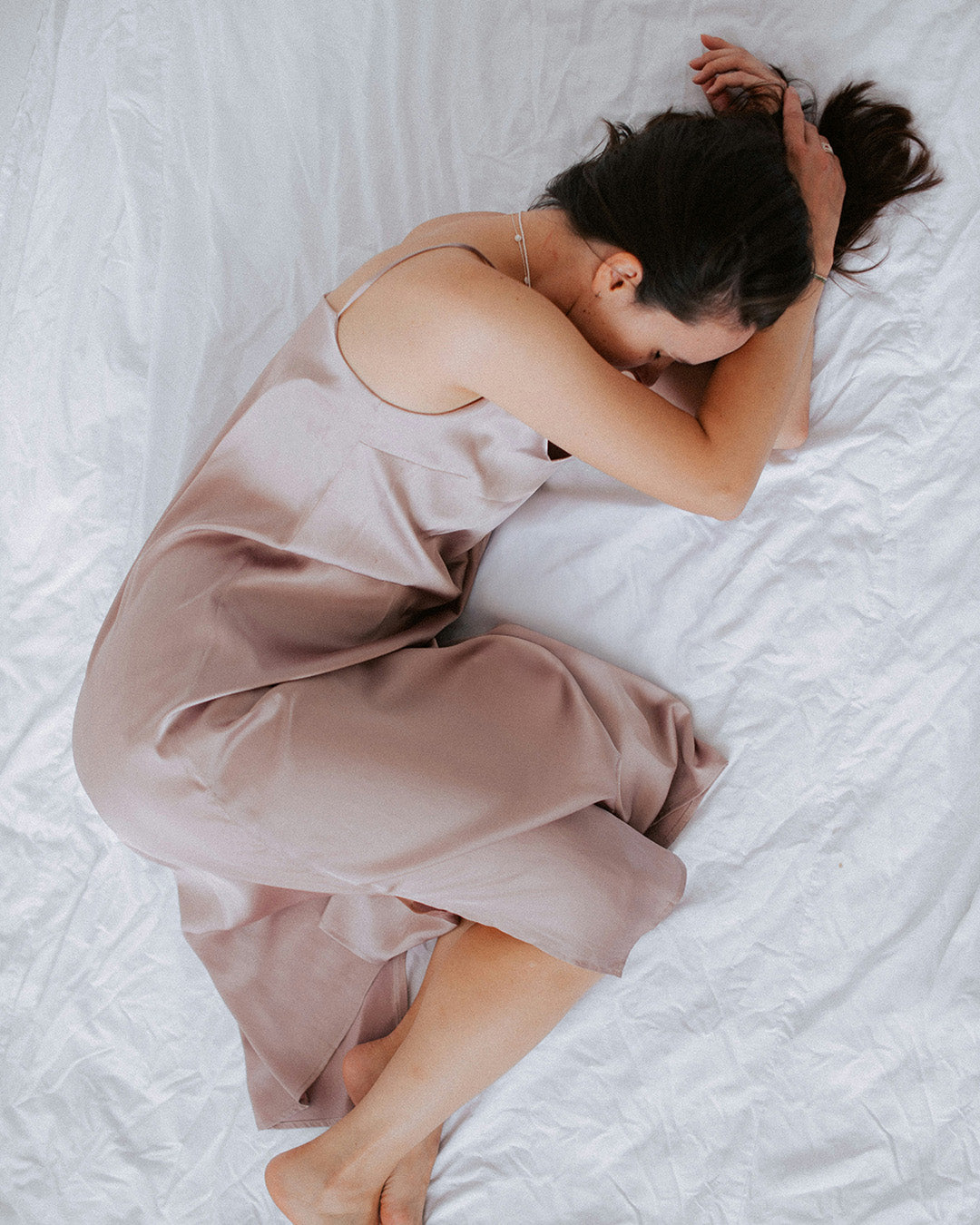 Woman in a beige satin nightgown lying on a white bed.